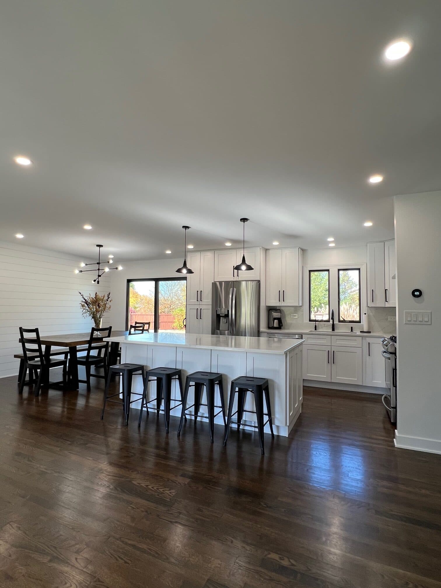 Open farmhouse kitchen and dining space with a shiplap accent wall and black industrial stools