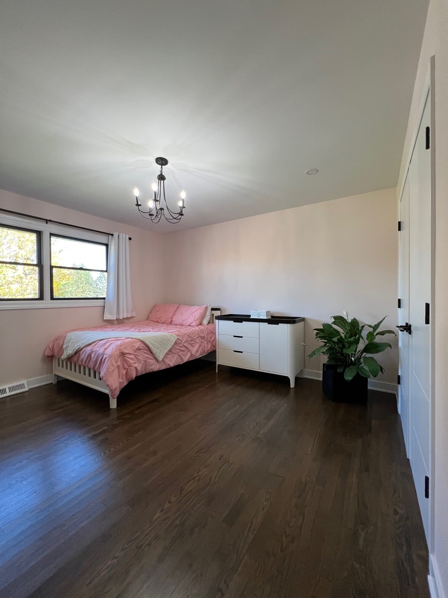Staged bedroom with blush pink bedding, a white spindle bed, and a candelabra chandelier